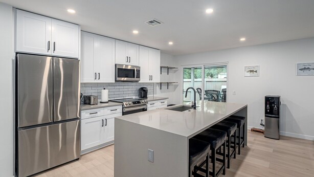 A modern kitchen with stainless steel appliances, white cabinetry, and a central island with bar stools. - 4Bdrm 3ba Pickleball, Pool Table, Nearby Marina! (Kingston)