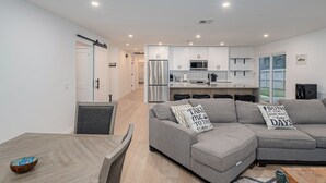 A modern living room with a grey sectional sofa, a dining table with chairs, and a kitchen in the background. - 4Bdrm 3ba Pickleball, Pool Table, Nearby Marina! (Kingston)