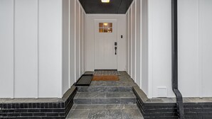 A narrow hallway with a white door at the end, a black pipe running along the wall, and a black mat at the bottom of the steps. - 4Bdrm 3ba Pickleball, Pool Table, Nearby Marina! (Kingston)