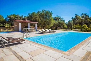 A rectangular swimming pool with clear blue water, surrounded by lounge chairs and a small pavilion with a tiled roof. - Villa Pomegranate Tree (Kefalonia)