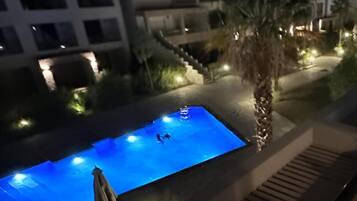 Ein Schwimmbecken mit zwei Personen, umgeben von Palmen und einem Gebäude mit vielen Fenstern.