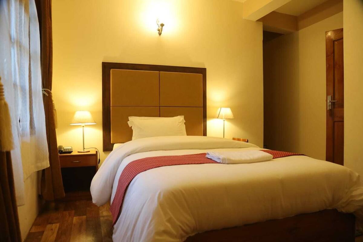 Ein Hotelzimmer mit einem großen Bett, zwei Nachttischlampen, einem Holz-Kopfteil und einer Tür auf der rechten Seite.
