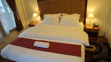 Une chambre d’hôtel avec un grand lit, deux tables de chevet avec des lampes, une fenêtre avec des rideaux et un tapis rouge sur le lit.