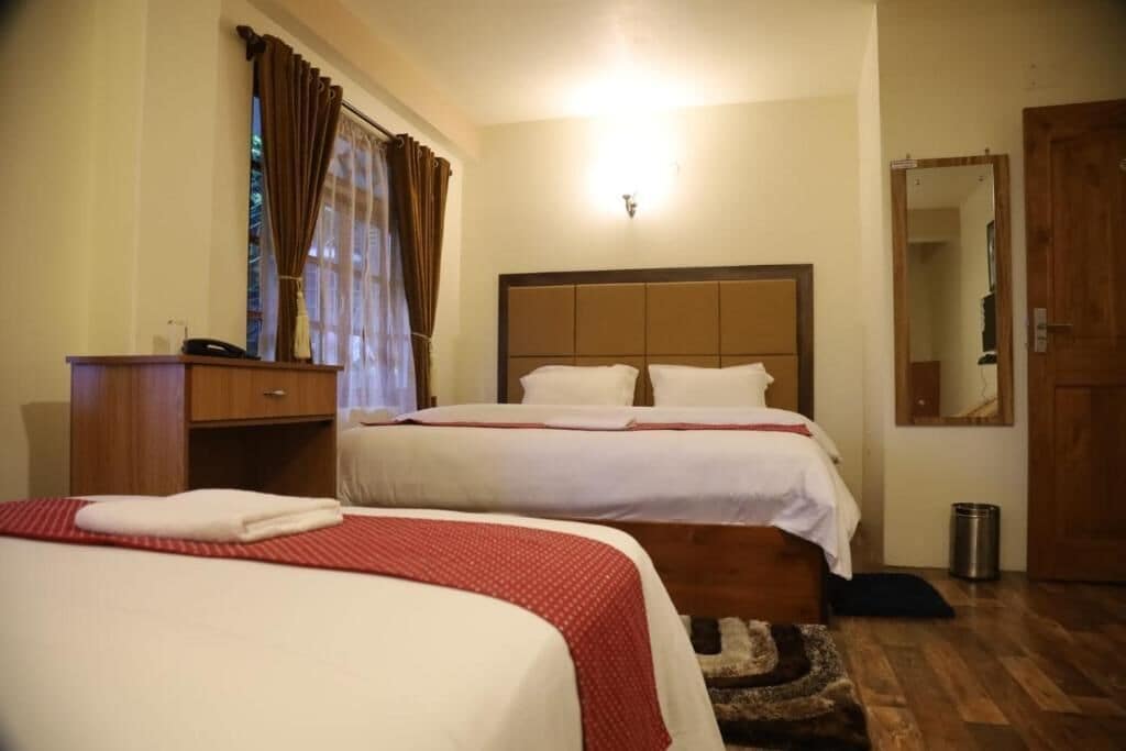 Habitación de hotel con dos camas, cabecero de madera, mesita de noche con teléfono y espejo en la pared.