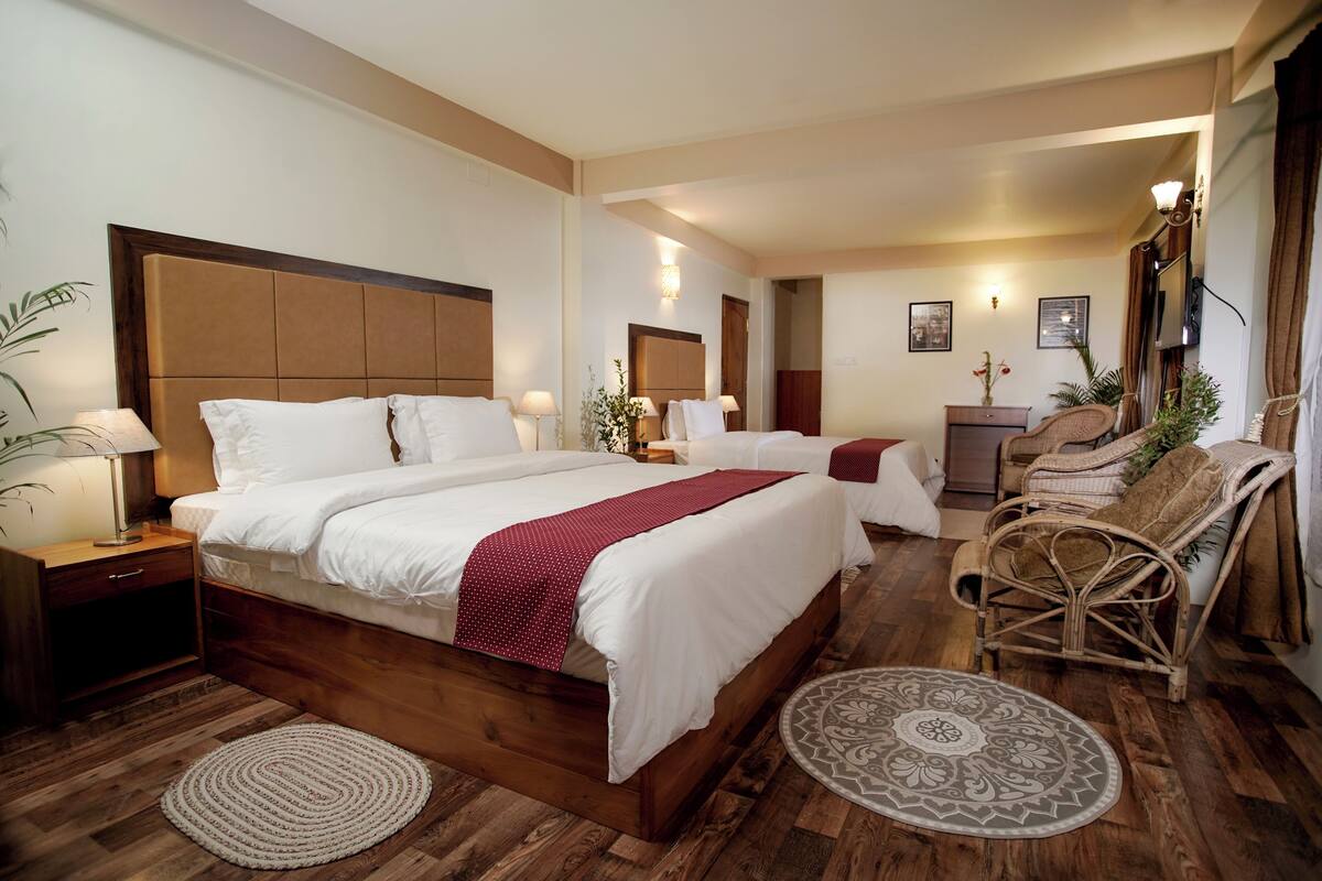 Ein Hotelzimmer mit einem großen Bett, zwei Nachttischen, einem Sessel, einem kleinen Schreibtisch und einem Fernseher.