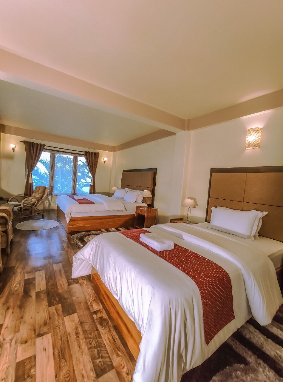 A hotel room with two beds, a sitting area with a chair, and a view of the outdoors.