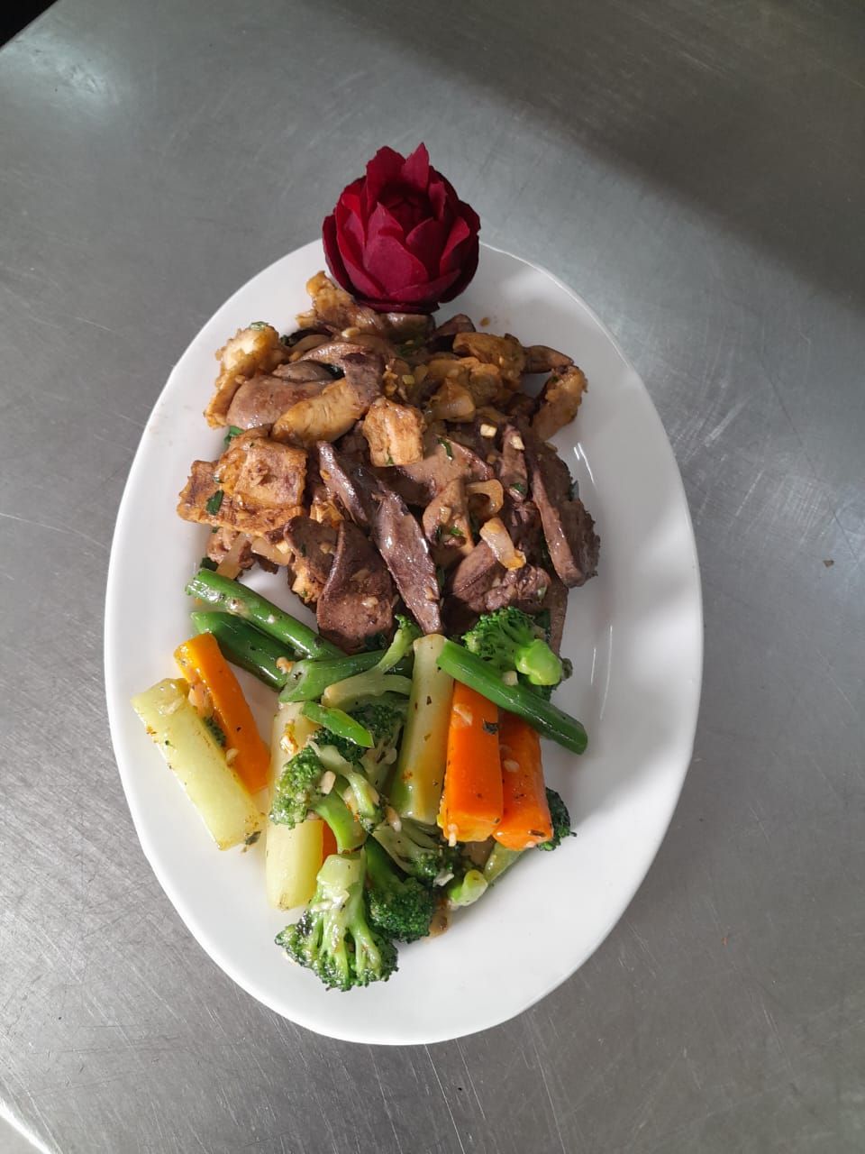 Un plato blanco con una variedad de alimentos, incluyendo carne, verduras y una flor roja como adorno.