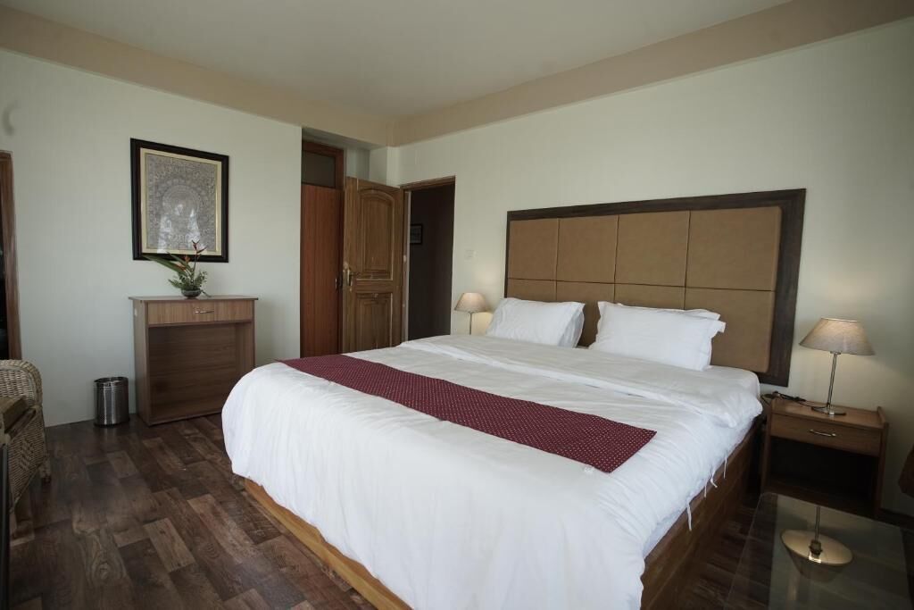 A hotel room with a large bed, wooden headboard, bedside tables with lamps, a small cabinet, and a framed picture on the wall.