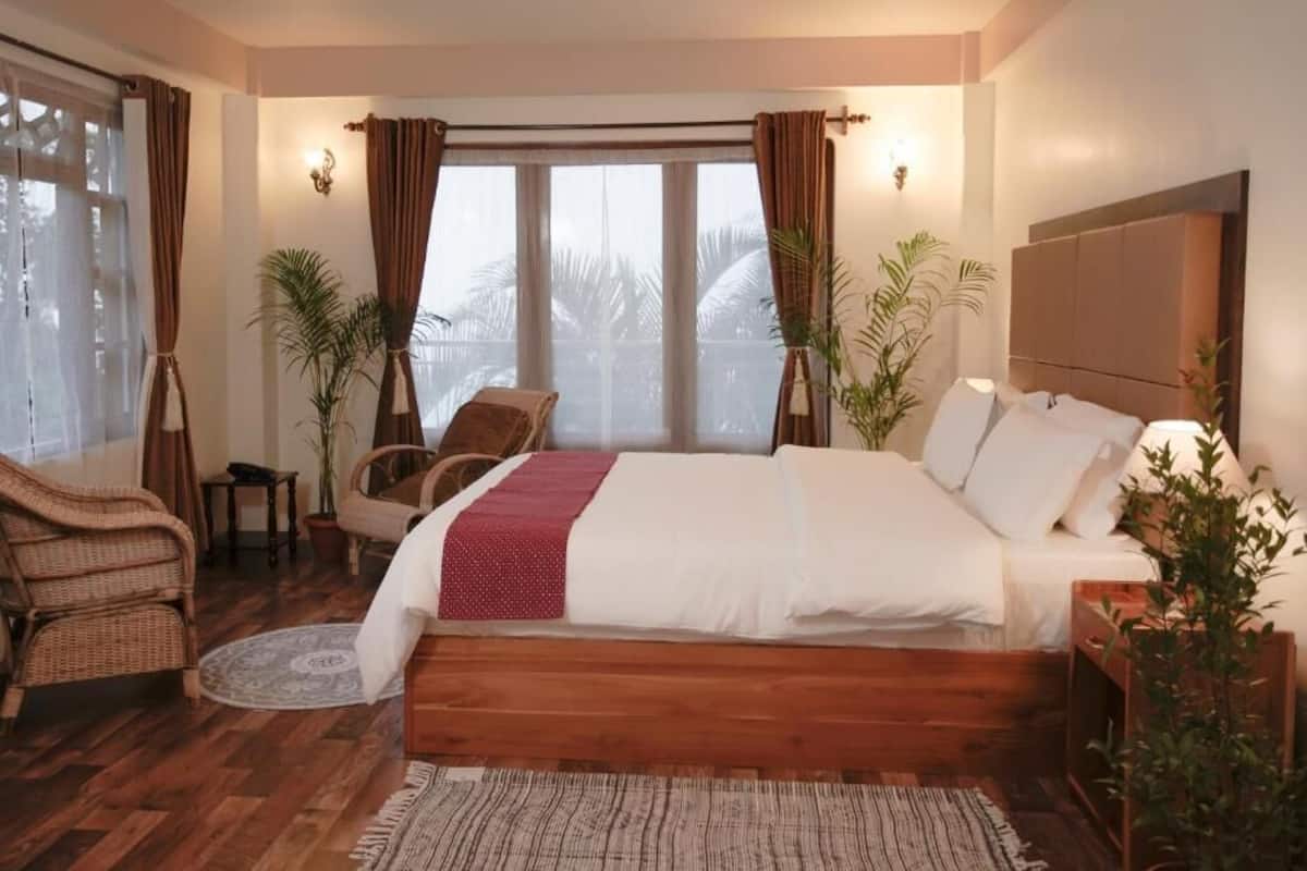 Ein Schlafzimmer mit einem hölzernen Bett, einer Sitzecke mit Sessel und kleinem Tisch sowie zwei Topfpflanzen.