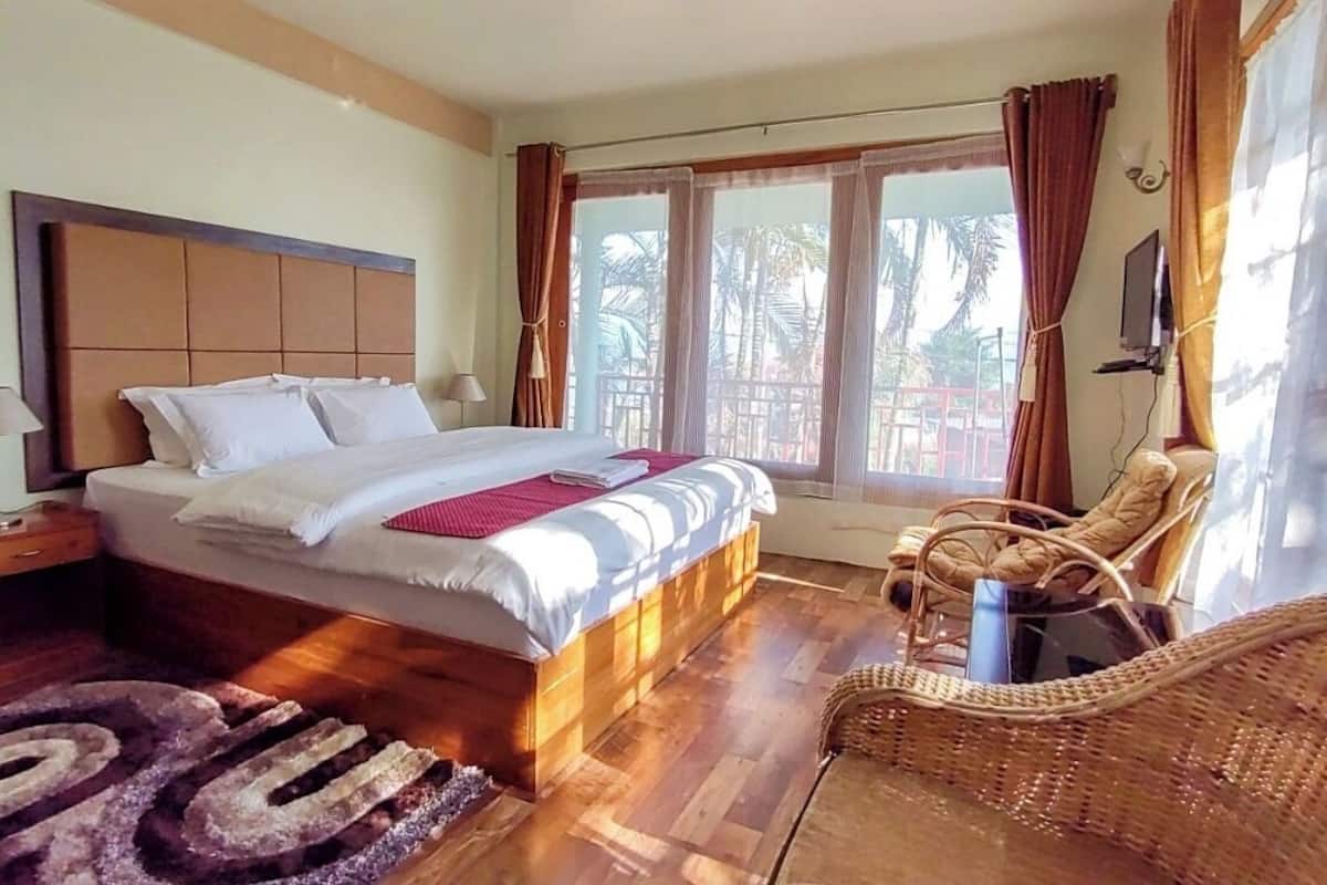 Ein Schlafzimmer mit einem großen Bett, einem Nachttisch, einem Sessel und einem Fenster mit Vorhängen.