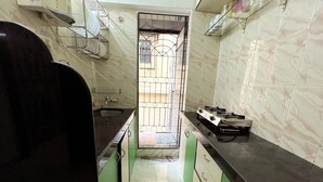 A narrow kitchen with a gas stove, a sink, and a window with a metal grill. - Quiet and Cozy 2 bed 1 bath in Bandra Near Ocean side
 (Mumbai)