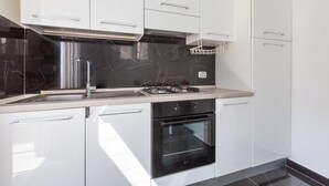 A modern kitchen with white cabinets, a black marble backsplash, a stainless steel range hood, and a built-in oven. - 3877 Dalie - Monolocale by Barbarhouse (Manduria)
