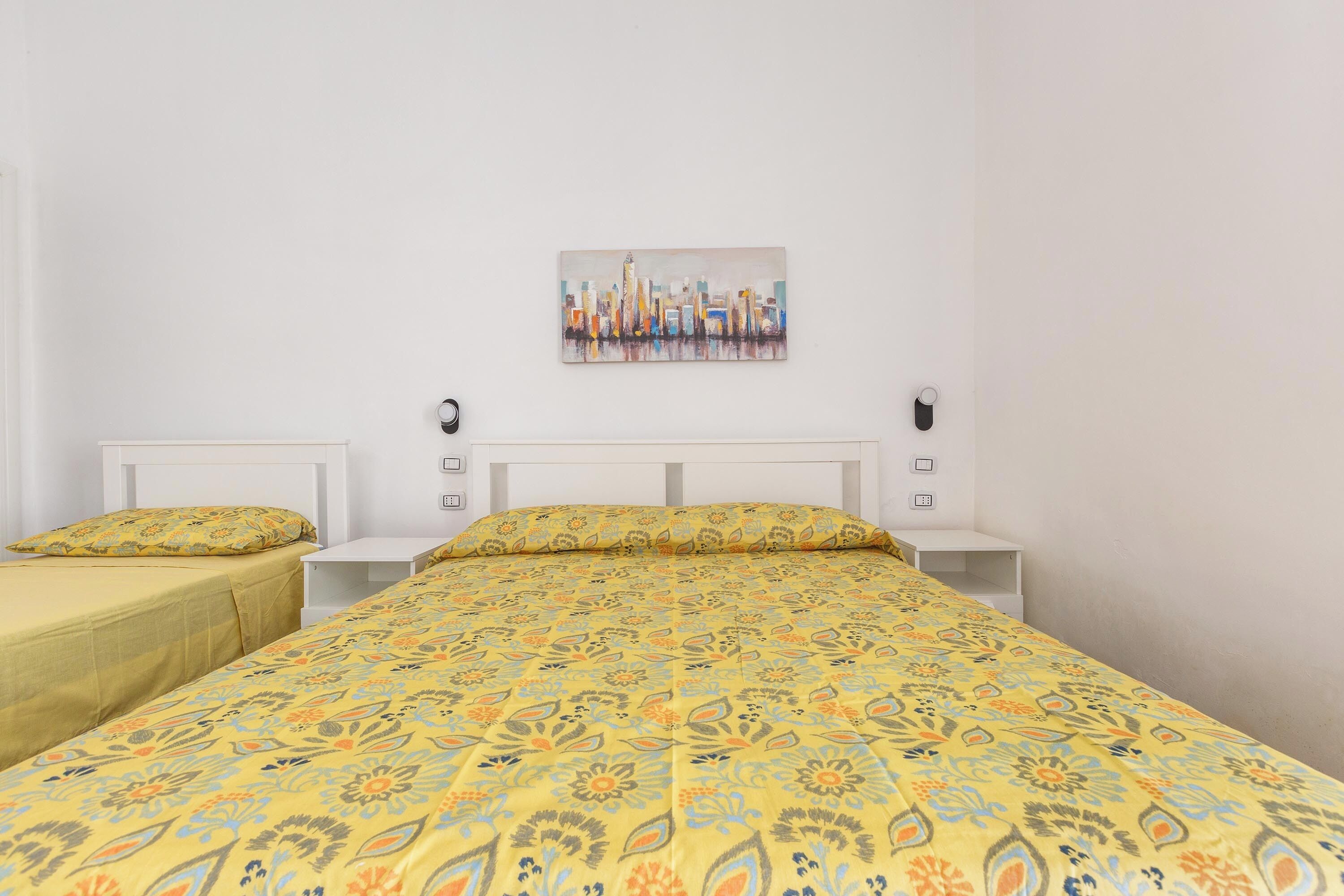 Hotelkamer met twee enkele bedden, een groot bed met een bloemenbedekking, een stadsgezichtschilderij aan de muur en witte hoofdeinden.