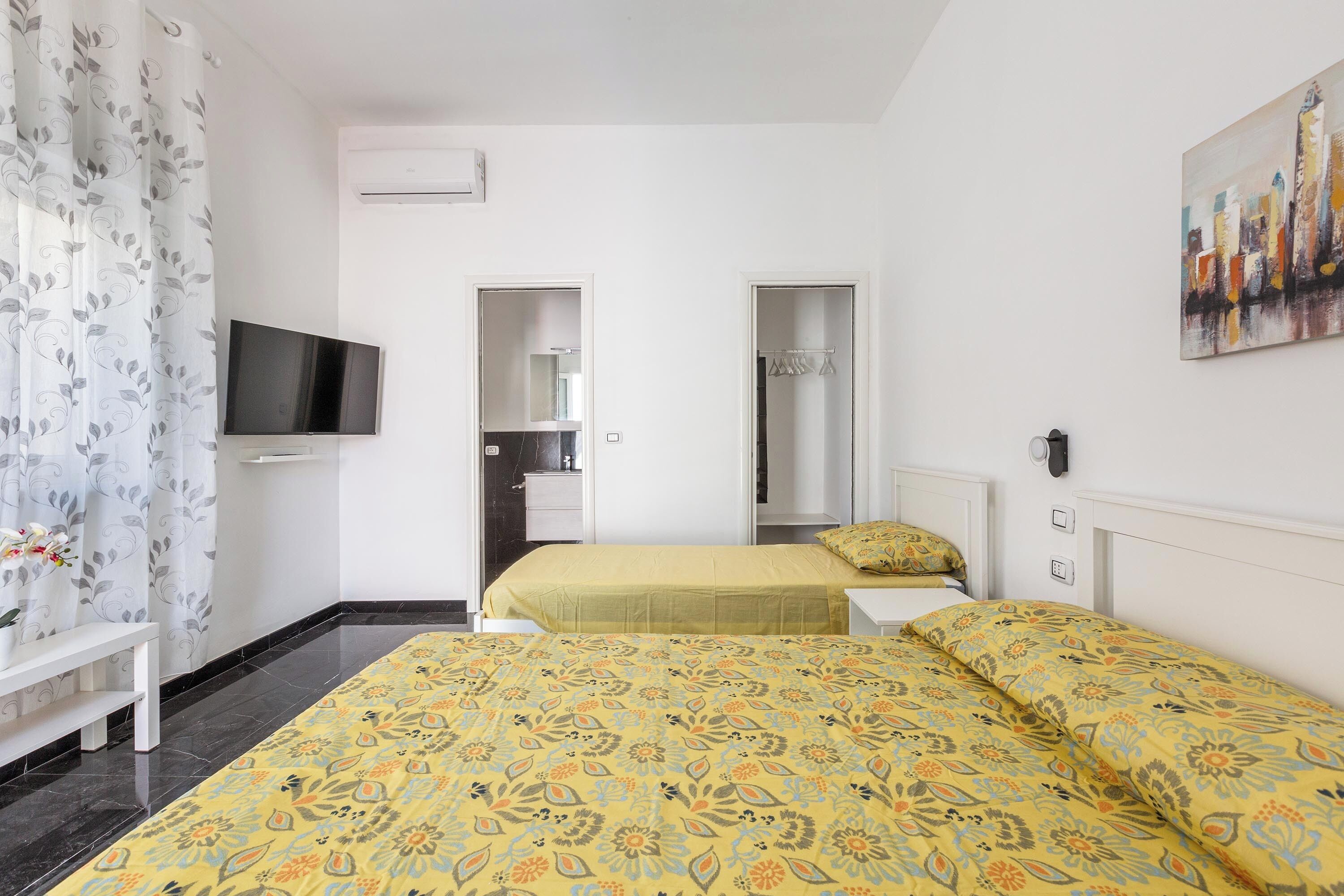 A hotel room with a bed, a TV, a bathroom, and a painting on the wall.