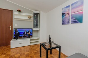 Una sala de estar con una televisión de pantalla plana, una botella de vino y copas sobre una mesa. Hay estantes con adornos y una puerta.