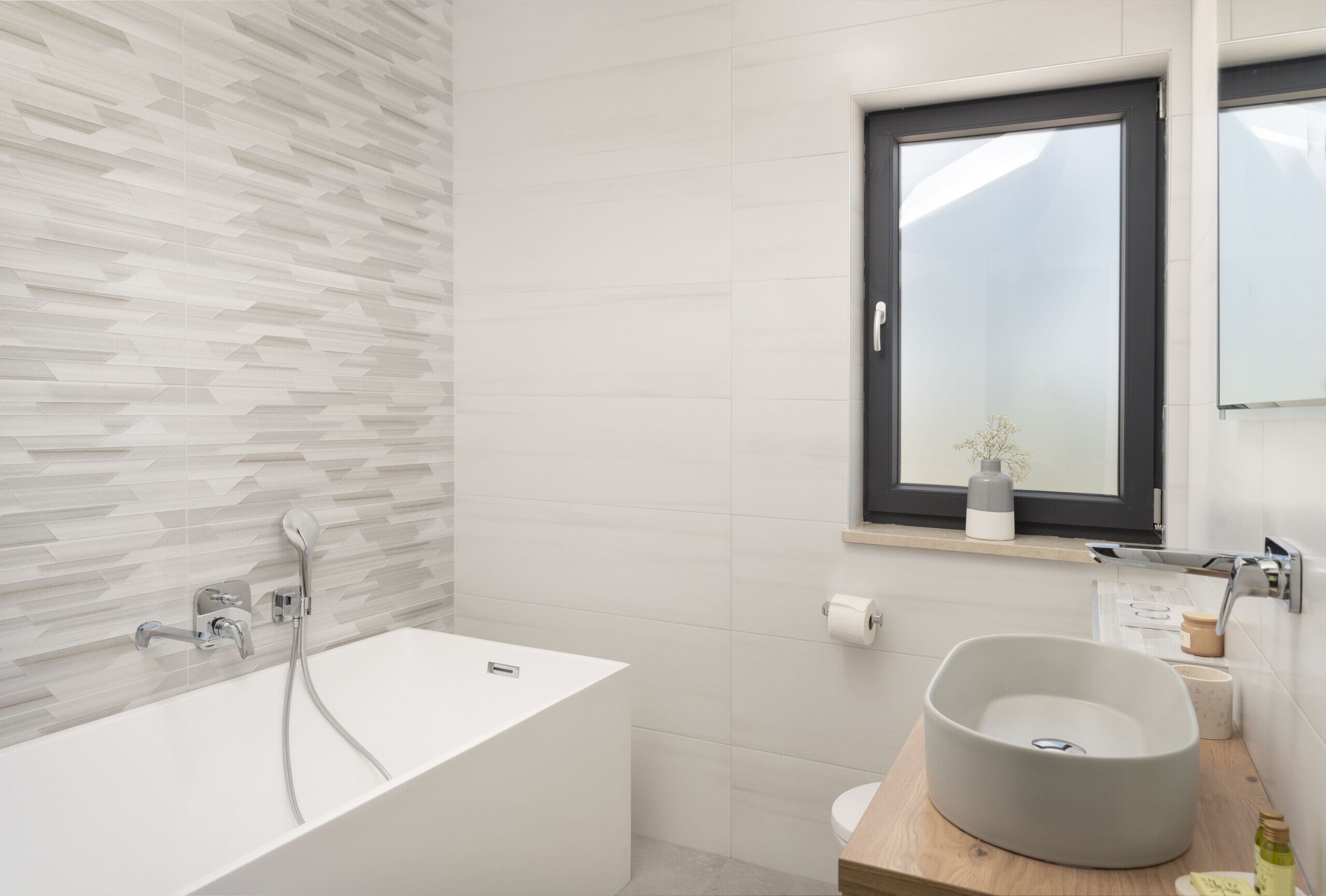 A modern bathroom with a freestanding bathtub, a round sink, and a window with a plant.
