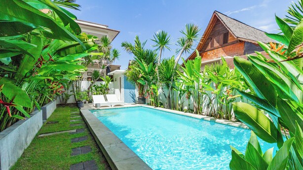 A swimming pool surrounded by lush greenery and a traditional wooden building. - Belvilla Aranya Sanur Beach (Denpasar)