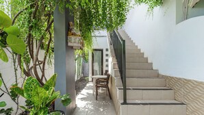 A narrow outdoor corridor with a staircase, potted plants, and a small table with chairs. - Belvilla Aranya Sanur Beach (Denpasar)