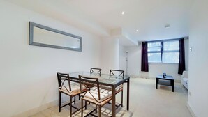 A dining area with a glass-top table and four chairs, a sofa, a small table, and a window with curtains.
