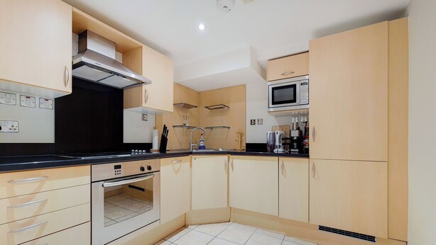 A modern kitchen with beige cabinetry, a built-in oven, a microwave, and a stainless steel range hood.