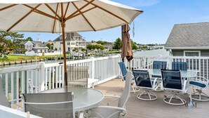 En terrasse med udendørs møbler, en hvid parasol og udsigt til huse og vand.