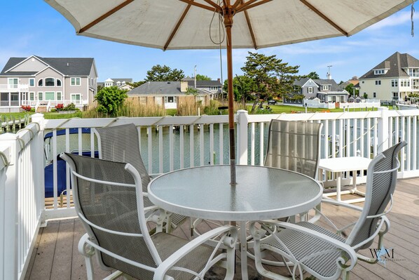 A patio with a round table and chairs, a large umbrella, and a view of houses in the background.
