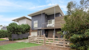 A modern two-story house with a flat roof, a balcony, and a fenced yard.