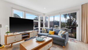 A modern living room with a flat-screen TV, grey sofa, and wooden coffee table.