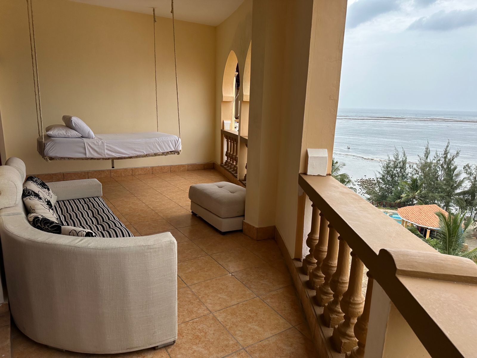 A balcony with a sofa, a hanging bed, and a view of the sea.