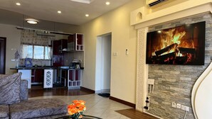 A modern living room with a sofa, a glass coffee table with a fruit design, and a fireplace with a fire. - The Penthouse Waterfronts (Mombasa)