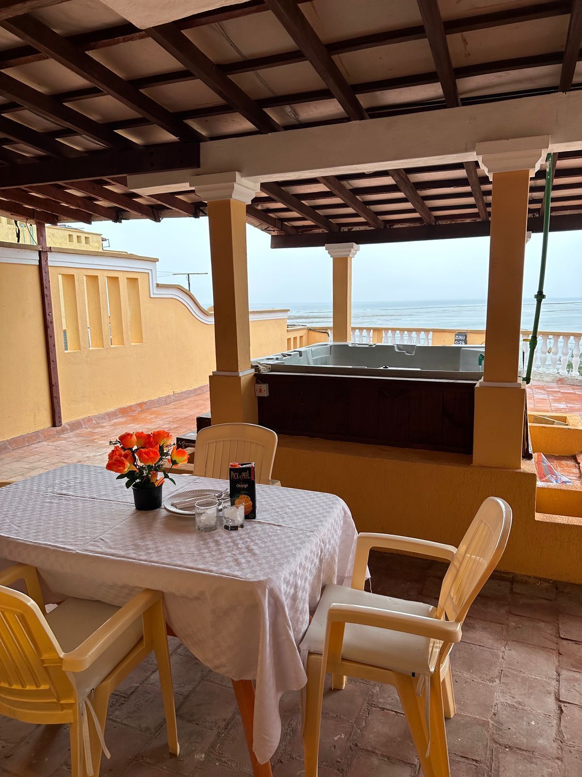 Un espace extérieur abrité, aménagé pour les repas, avec une table pour deux, un barbecue et une vue sur la mer.