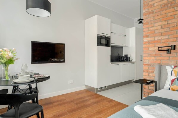 A modern kitchen with white cabinets, a microwave, and a coffee machine. There is a dining table with chairs and a vase of flowers.