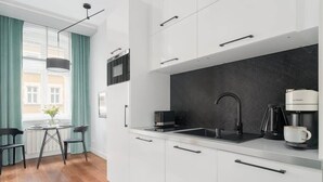 A modern kitchen with white cabinets, a black countertop, and a coffee machine. - Comfortable Studio in the Center | Close to the Old Market and WiFi (Poznan)