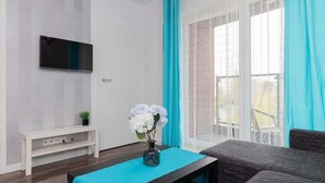 Un soggiorno moderno con una televisione a schermo piatto montata su una parete strutturata, un piccolo tavolino consolle bianco, un tavolino blu decorativo e un divano grigio.