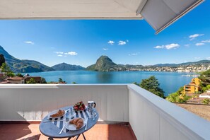 A balcony with a table set for breakfast, overlooking a lake and mountains. - Casa Serenella Splendid Lake View (Lugano)
