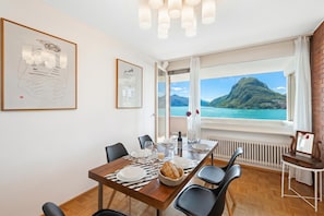 En matplats med ett bord dukat för fyra personer, utsikt över ett berg och en sjö samt konstverk på väggarna.