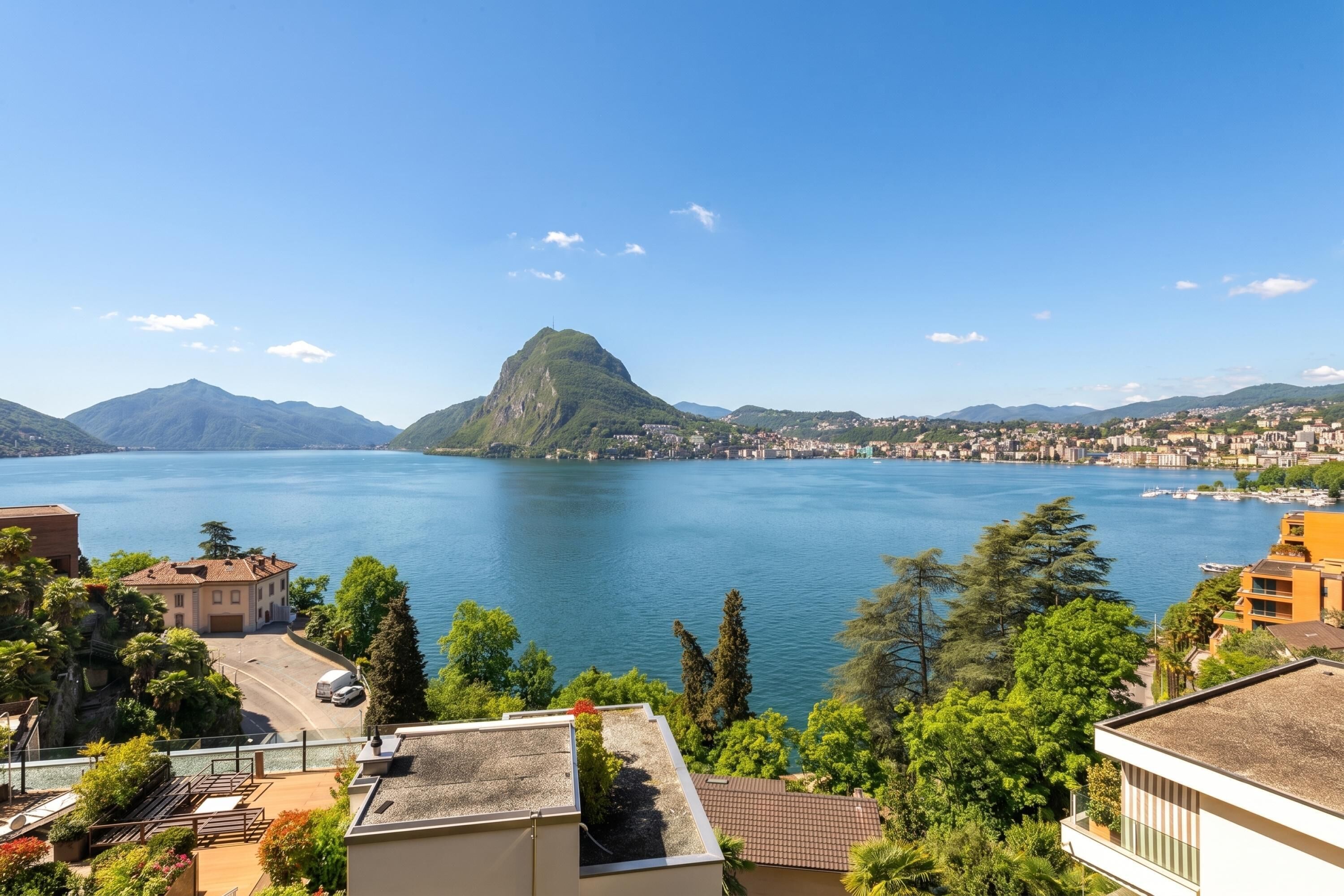 A lakeside view with a prominent mountain, residential buildings, and clear skies.