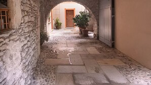 A stone-walled corridor with an arched doorway, potted plants, and a door in the distance. - Apartment in historic building - blue (Bedero)