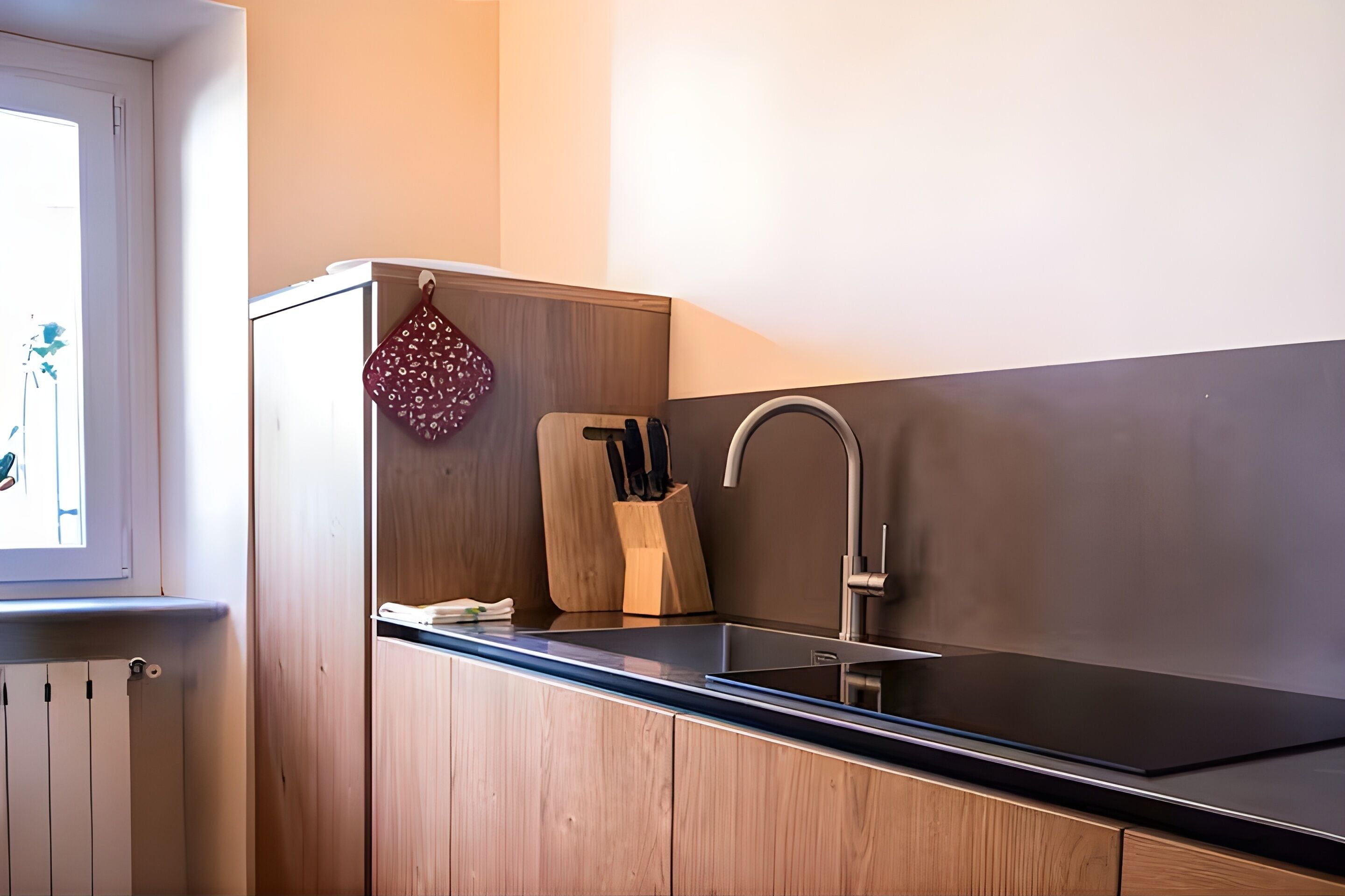 Una cocina moderna con encimera negra, armarios de madera, pileta de acero inoxidable y un colgador para ollas.
