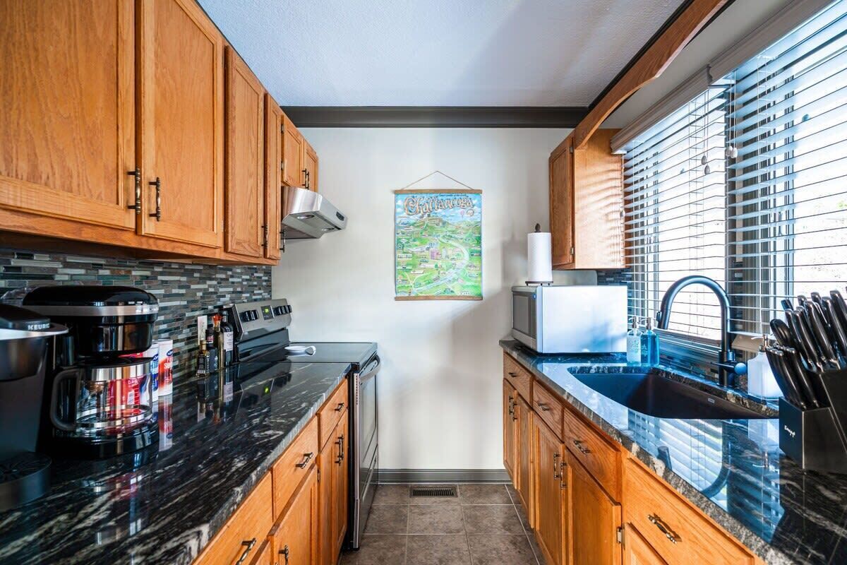 A kitchen with wooden cabinets, a black countertop, a coffee maker, a microwave, and a sink.