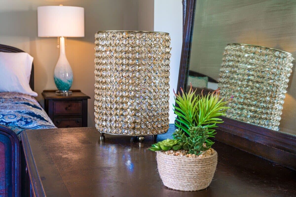 A room with a bed, a lamp, a decorative lamp, a mirror, and a potted plant.