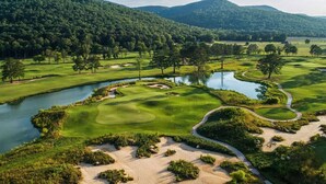 A golf course with water hazards, sand bunkers, and a mountainous backdrop. - The Loft - Lounge with Grill and Hot Tub! (South Pittsburg)
