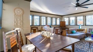 A spacious living room with a wooden dining table, comfortable seating, large windows, and a ceiling fan. - The Loft - Lounge with Grill and Hot Tub! (South Pittsburg)