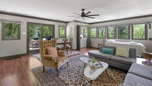 A spacious living area with a large window, a ceiling fan, and a dining area with a table and chairs. - The Loft - Lounge with Grill and Hot Tub! (South Pittsburg)