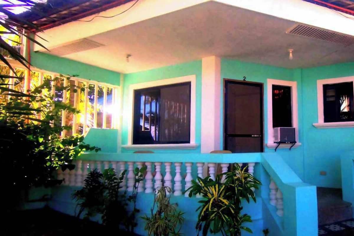 A two-story building with a light blue exterior, large windows, and a balcony with a white balustrade.