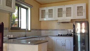 Cucina con isola centrale, mobili bianchi, frigorifero in acciaio inossidabile e finestra vista su spazi verdi.