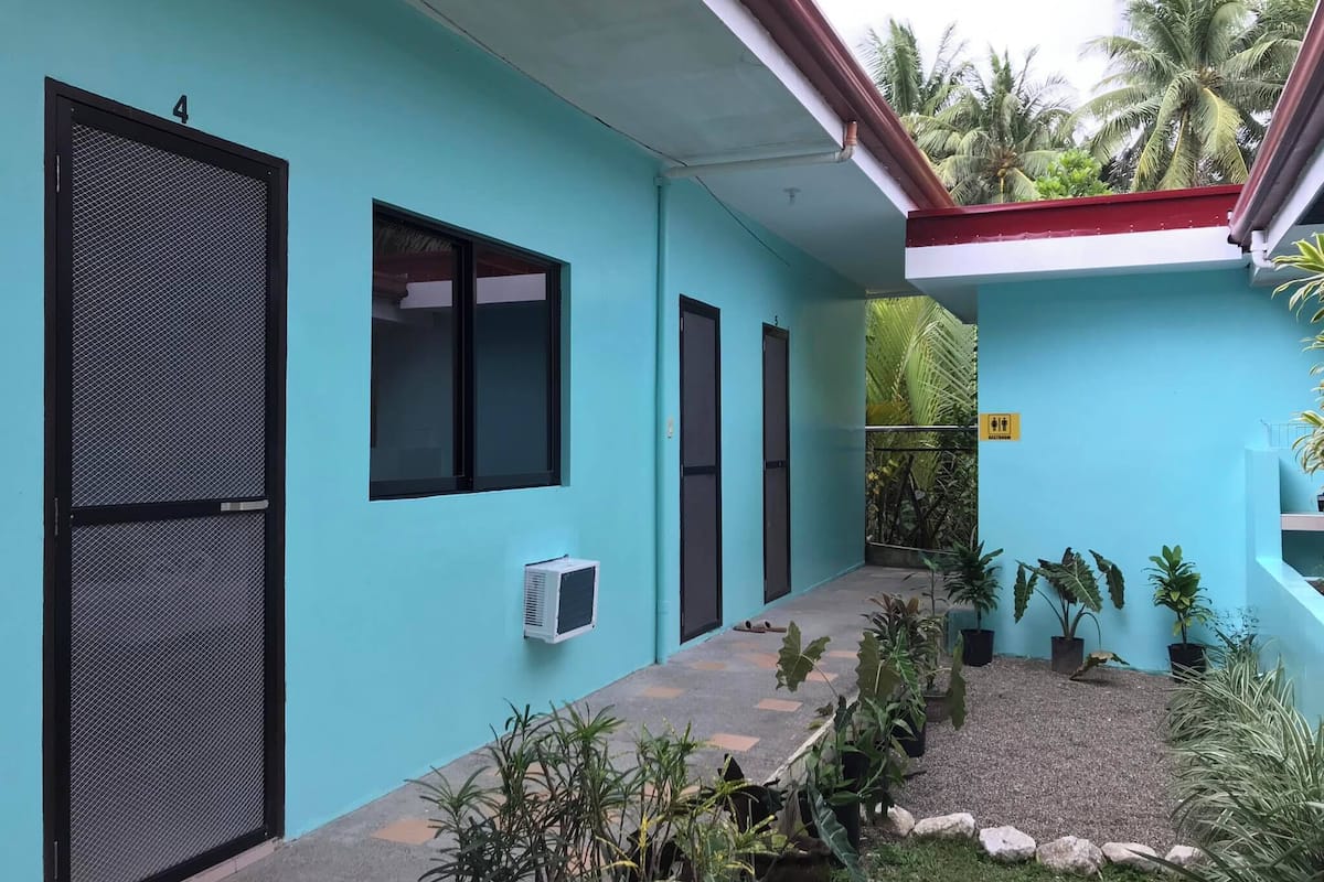 A building with teal walls, black mesh doors, and a small garden area with potted plants and a gravel path.