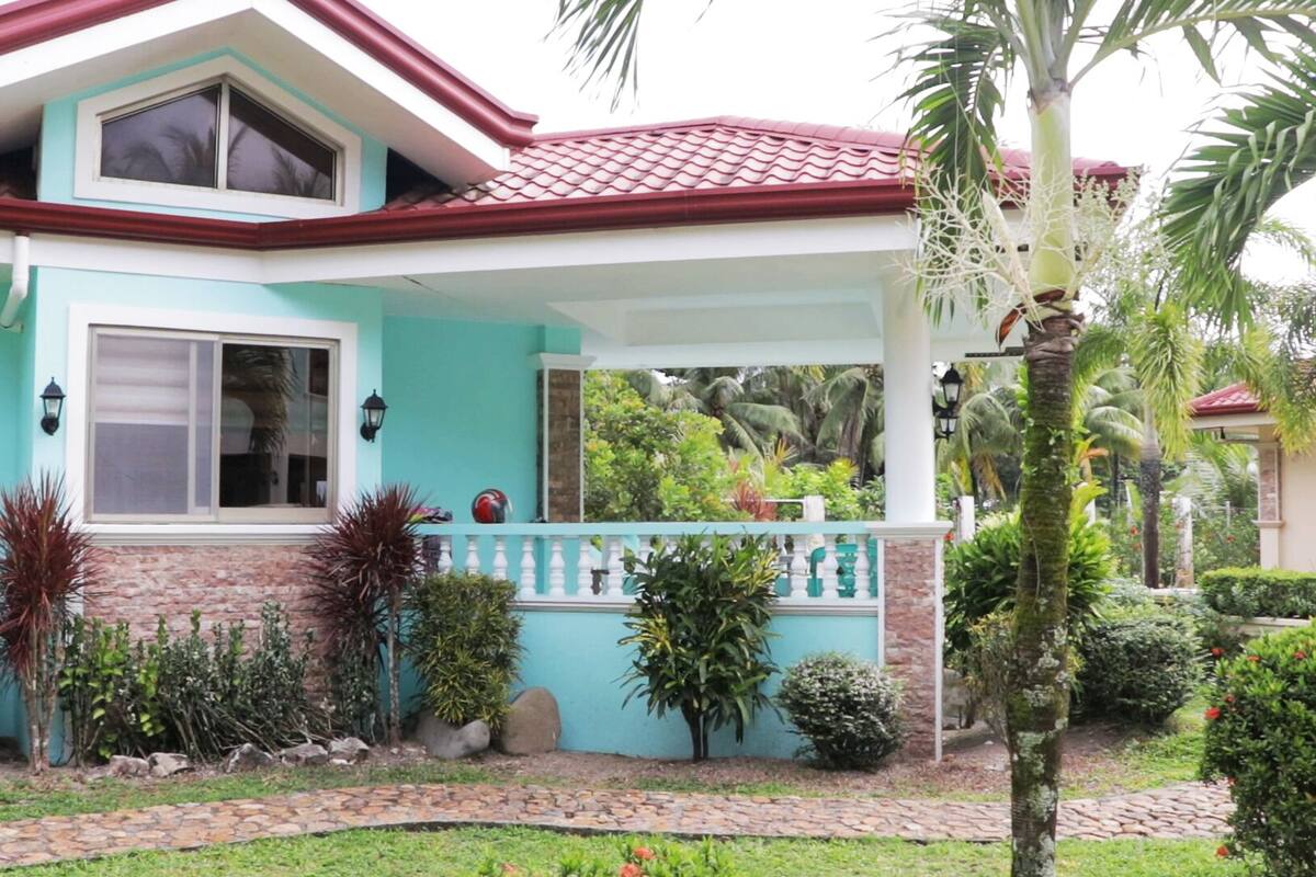A house with a red-tiled roof, a light blue exterior, and a small porch with a white railing.