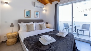 Una habitació d'hotel amb un llit gran, un sostre de fusta, un balcó amb cadires i vistes cap a l'exterior.