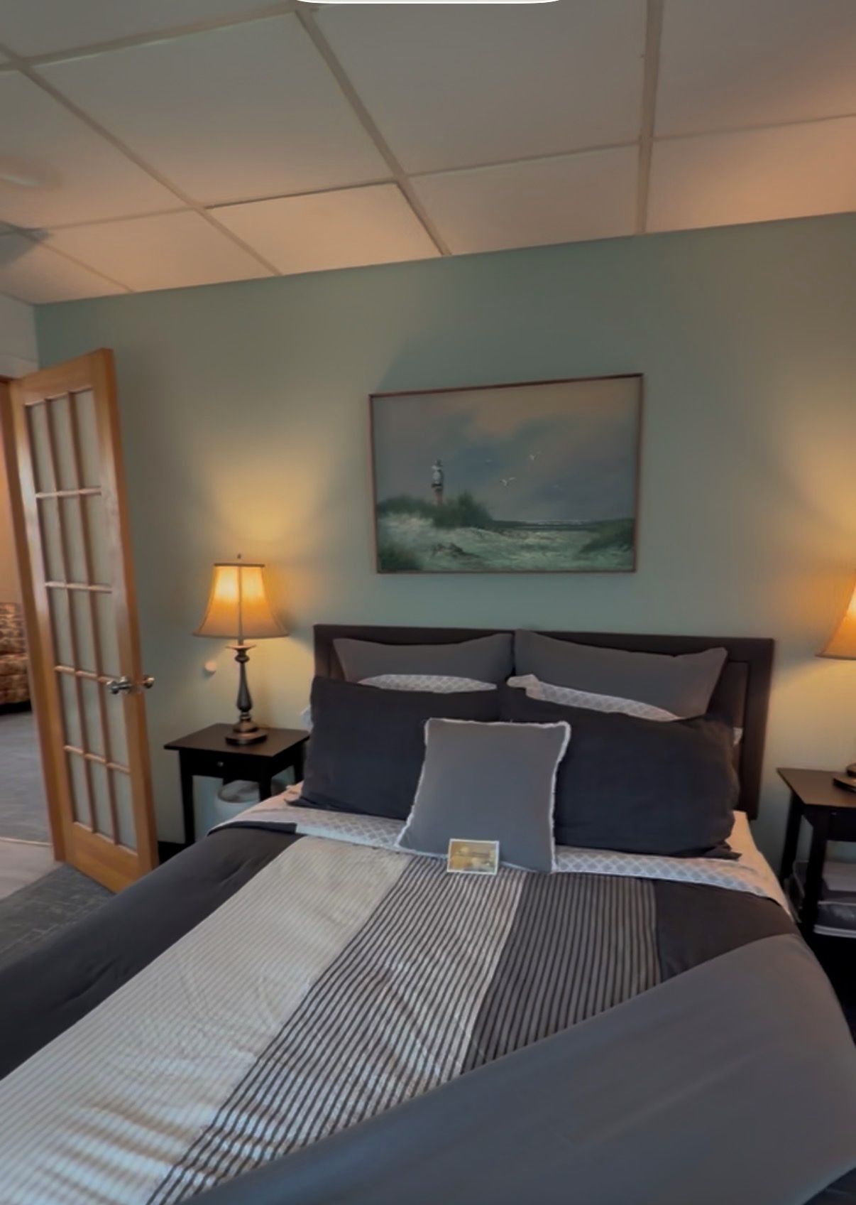 A bedroom with a bed, two bedside tables, a nightstand, a door, and a painting on the wall.